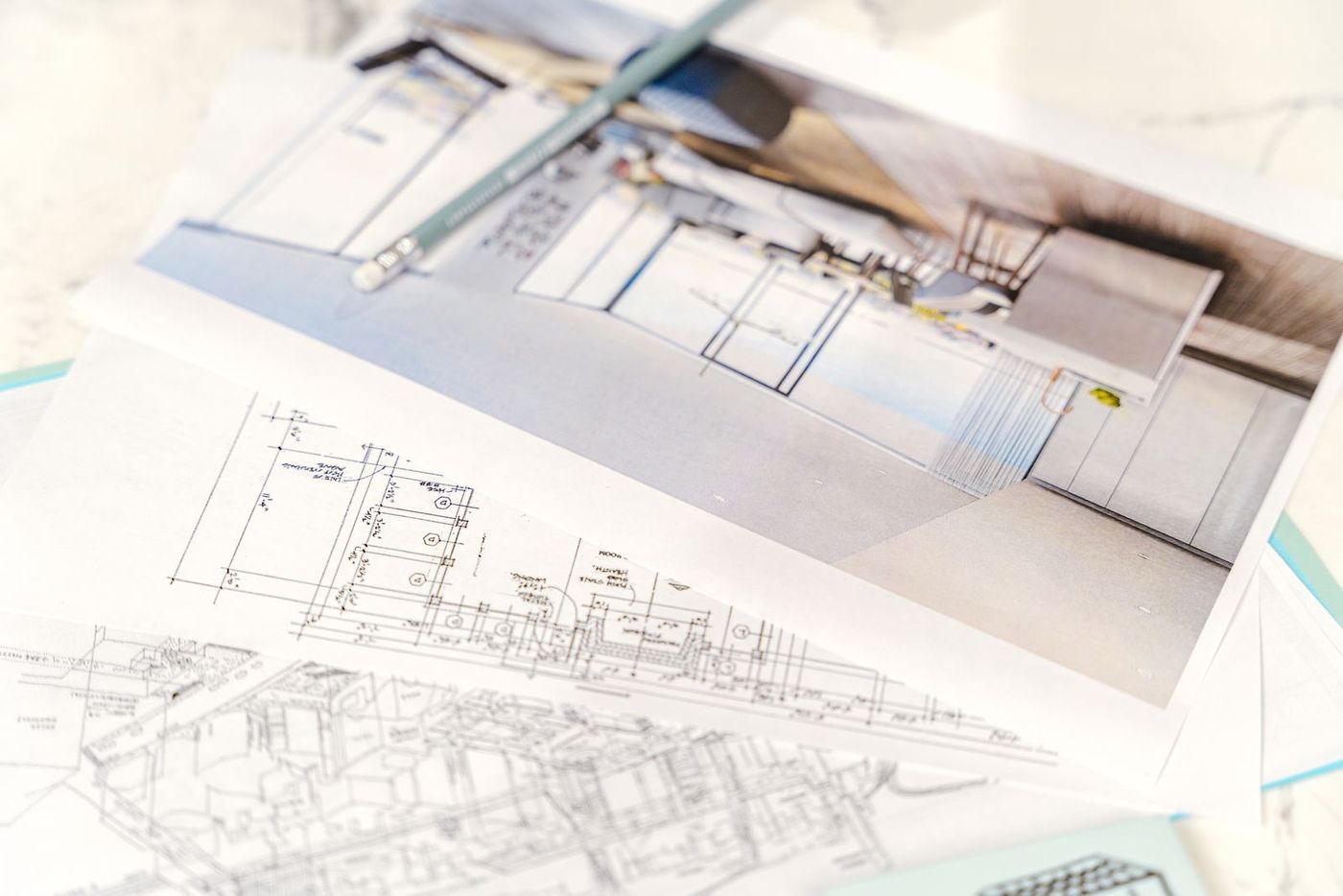 Architectural floor plans and 3D design drawings on a desk with a pencil