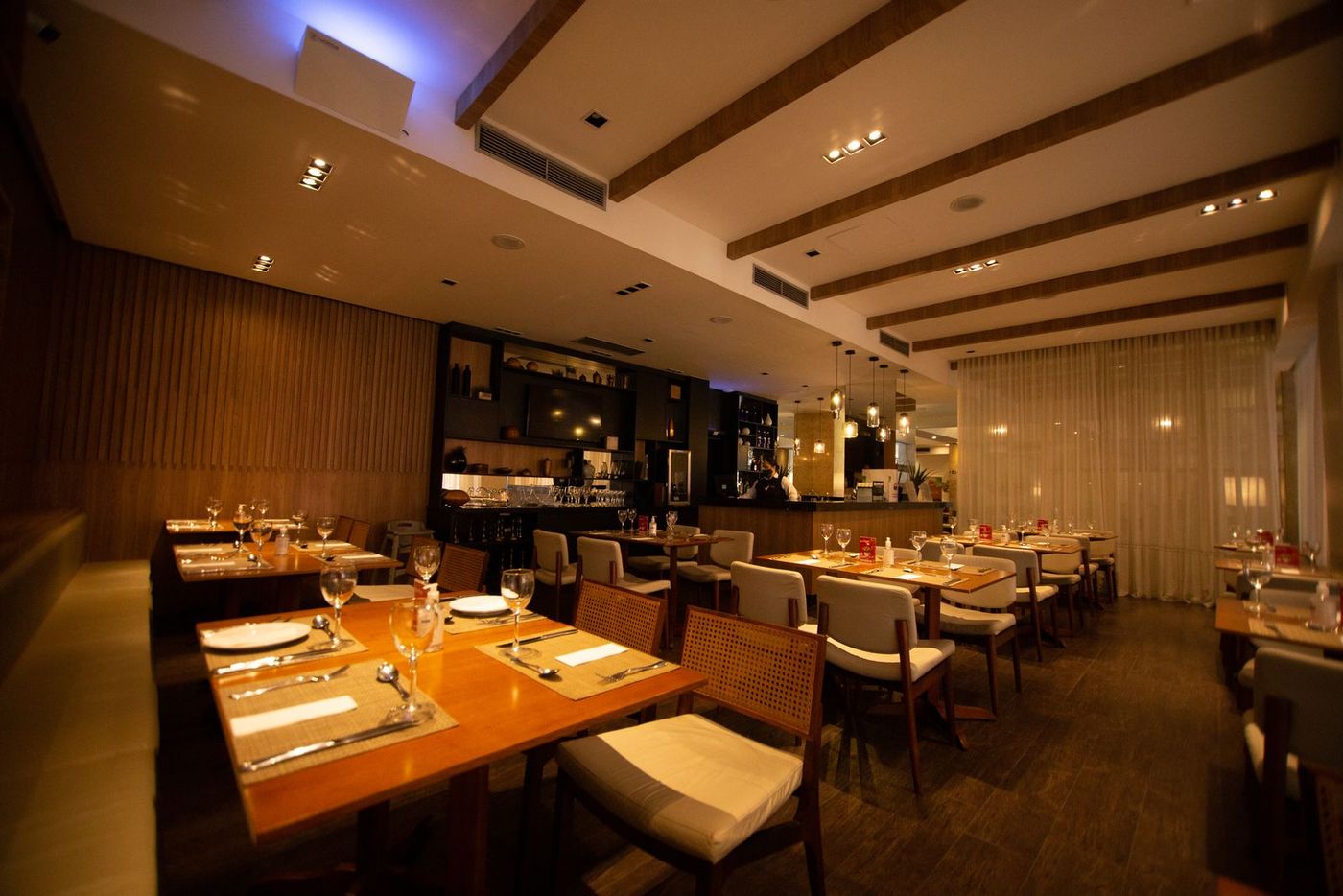 A warmly lit restaurant with laid tables, timber ceiling beams and a bar